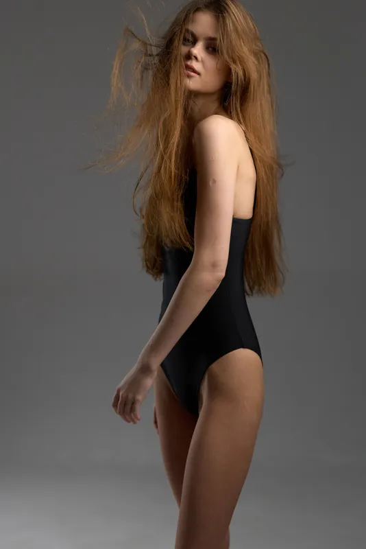 Portrait of slender woman with long hair wearing black bodysuit against gray background