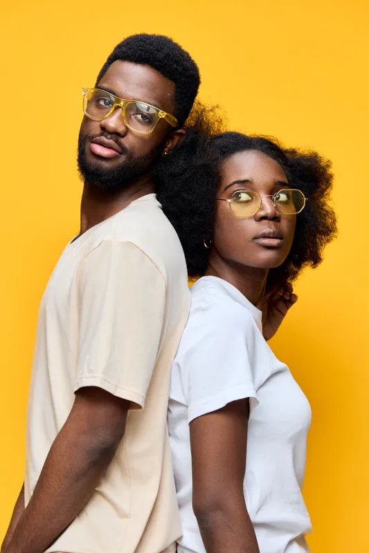 Stylish young couple with glasses against a vibrant yellow background, expressing confidence and joy, perfect for modern fashion and lifestyle concepts