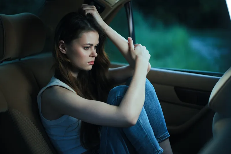 Pensive young woman sitting in a car, reflecting on life in a moody atmosphere with a focus on her emotions and dark color palette.