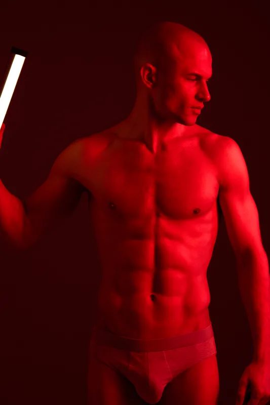 Athletic man posing confidently in a dramatic red light, showcasing his fit physique and expression. This striking image highlights strength and determination.