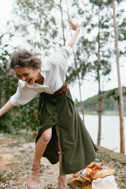 Young woman laughing joyfully outdoors in a white shirt and green skirt, surrounded by nature, conveying a sense of freedom and happiness