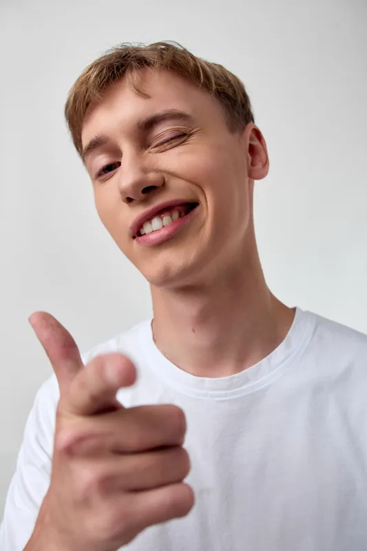 Pointing, smiling man in a casual white t-shirt delivers a confident message, close up shot for lifestyle, social media or marketing use, emphasizing engagement and direct communication