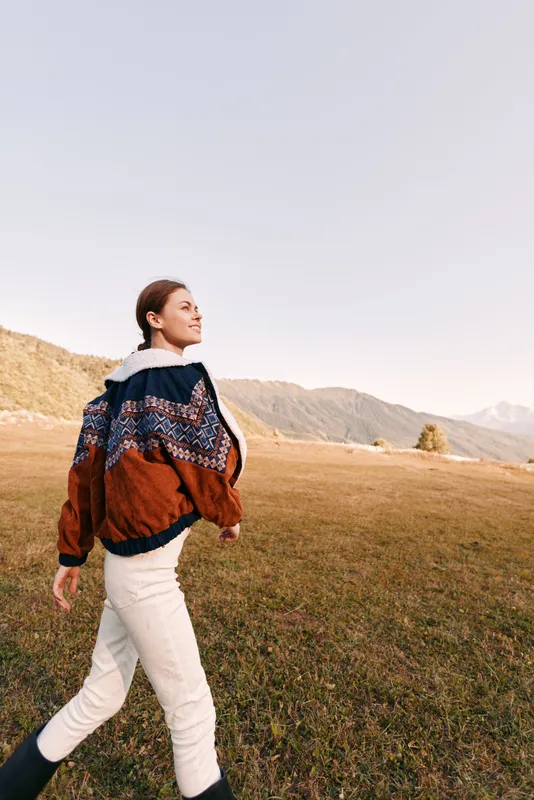 Woman walking in mountains meadow wearing patterned sweater and warm boots, enjoying autumn landscape and open field, outdoor lifestyle, travel and nature escape.