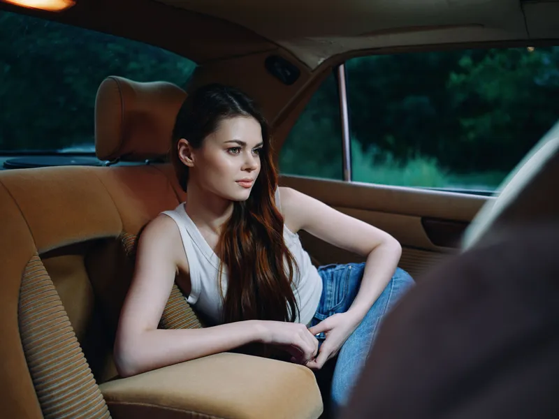 Young woman in casual attire relaxing in a vintage car interior, showcasing a serene expression and fashion-forward style, ideal for lifestyle and travel content.