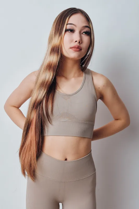 Young woman with long brown hair wearing beige sportswear posing with hands on hips against white background for fitness, health and lifestyle concept.