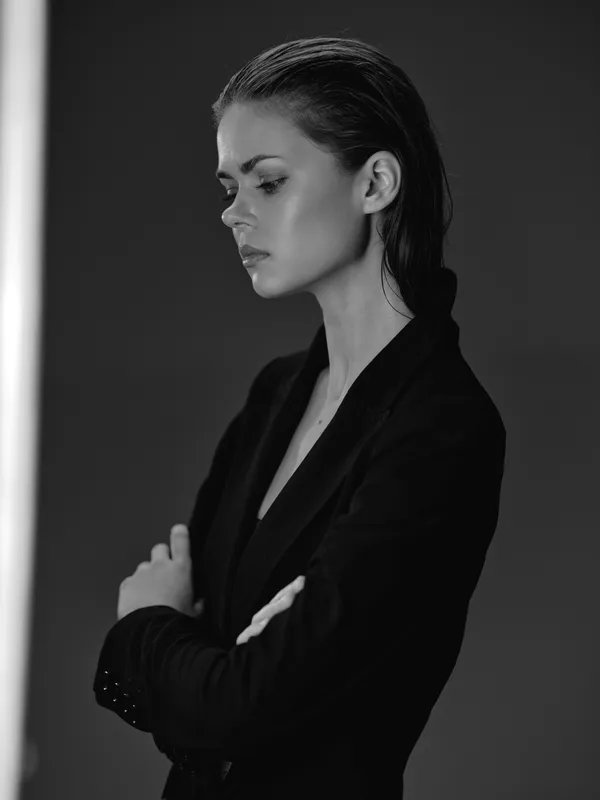 Black and white portrait of a serious woman in a dark blazer with wet hair and crossed arms, showing confidence and elegance.