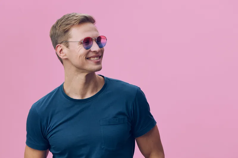 Smiling young man wearing sunglasses blue t-shirt standing look aside isolated on pink background casual style happiness concept