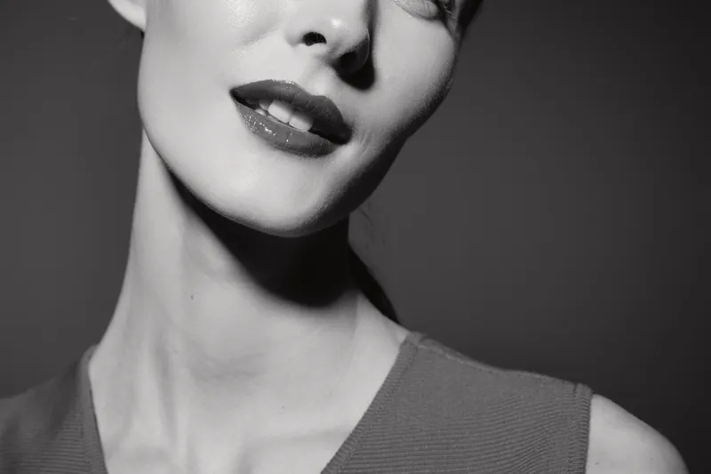 Close-up black and white portrait of a young caucasian woman with fair skin showing smile and neck in studio. Concept of beauty, elegance, and female facial expression.