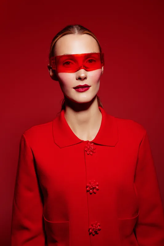 Portrait of a woman wearing a red sweater and red translucent glasses against a red background. Concept of fashion, style, and monochrome color theme with modern accessories.