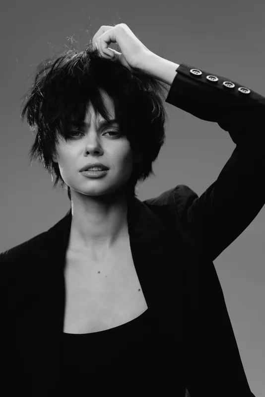 Black and white portrait of a woman with tousled hair wearing a dark blazer with buttons