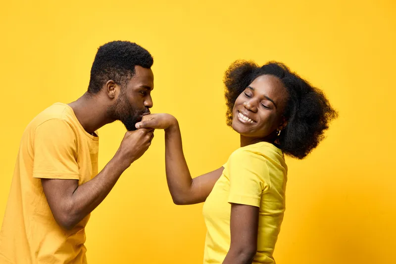 Young African couple sharing a romantic moment in matching yellow outfits against a bright yellow background, showcasing love and joy in a playful setting