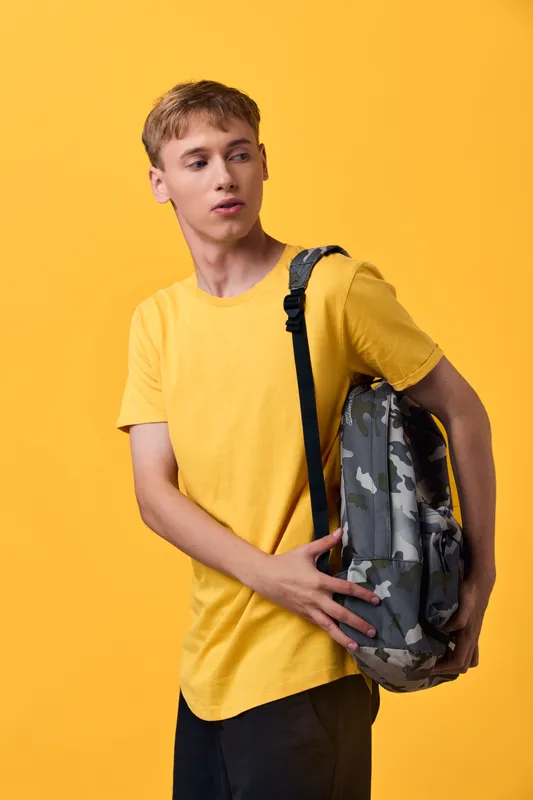 Backpack youth casual fashion travel student yellow shirt camouflage backpack slung over shoulder as a stylish young man looks aside, capturing urban lifestyle and ready for everyday adventures