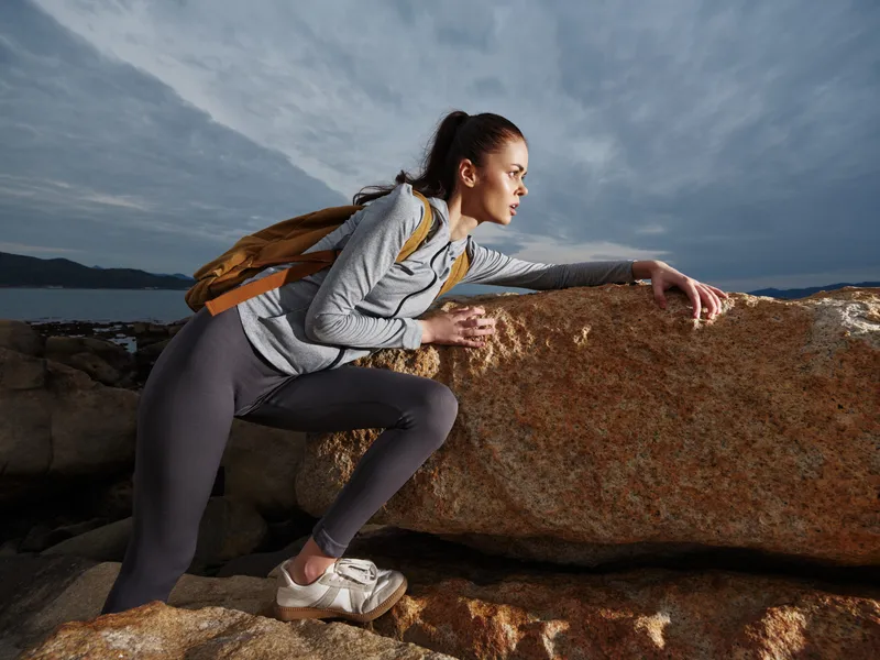 Young female hiker climbing on rocky terrain during overcast day, showcasing determination and adventure in outdoor exploration
