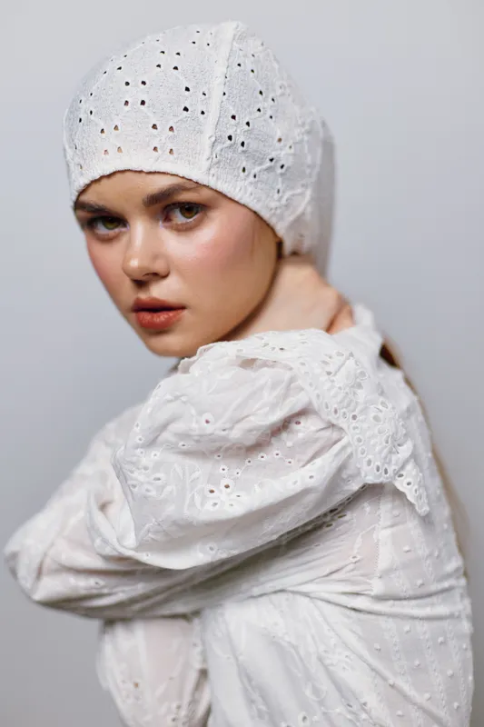 Young woman in a white embroidered headscarf and dress, expressing beauty and elegance against a neutral background, showcasing a fresh, ethereal vibe