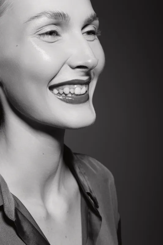 Close-up portrait of a smiling Caucasian woman with fair skin and glossy lips on dark background. Concept of happiness, beauty, and natural expression in monochrome.