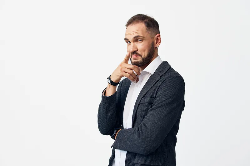Professional man in a smart casual jacket and white shirt stands against an isolated white background, projecting confidence, focus, and calm leadership in a thoughtful pose.