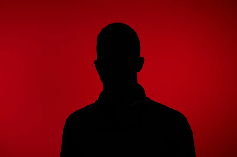 Dark silhouette of a person with a red background, symbolizing mystery and intrigue, ideal for concepts related to identity, anonymity, or hidden emotions
