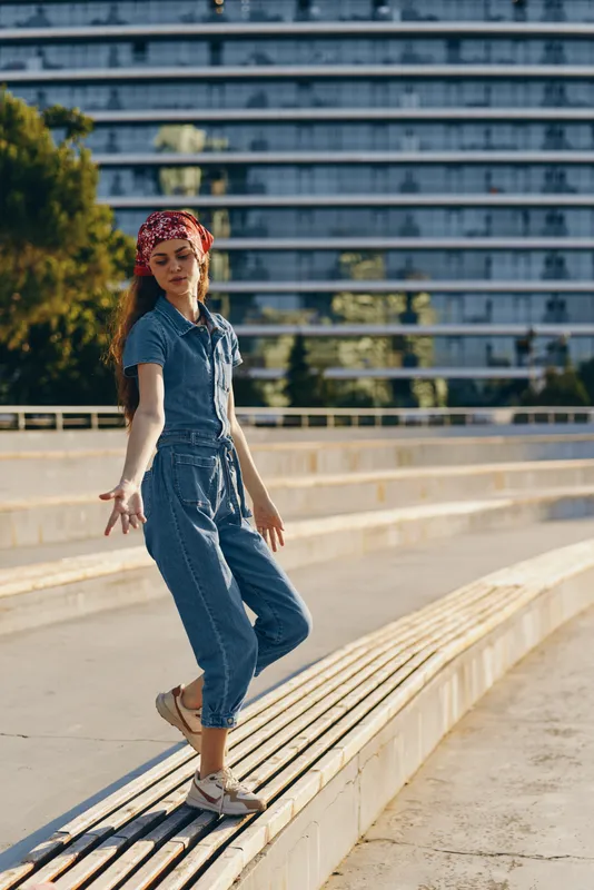Lifestyle woman in modern boho-western denim street style wearing a red bandana, relaxed pose, warm film color tones, urban outdoor background, casual summer fashion.