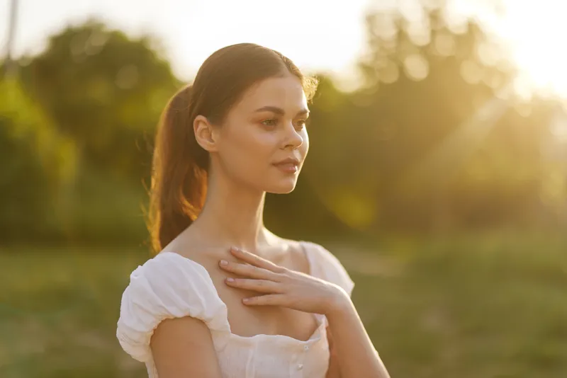 Young woman in white dress, enjoying sunset in serene outdoor setting, conveying feelings of peace and reflection, ideal for concepts of self care and tranquility
