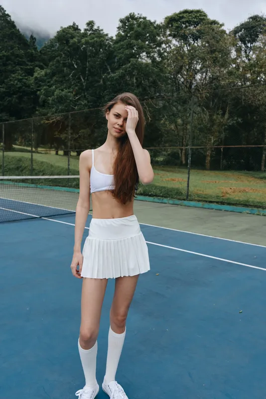 Stylish young female athlete in a white sports outfit on a tennis court, showcasing confidence and athleticism during a workout in nature