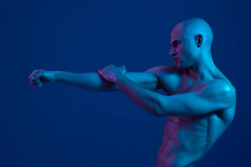 A thoughtful man in a contemporary style poses under vibrant blue lighting, showcasing a unique expression and strong physique in a striking human figure composition.