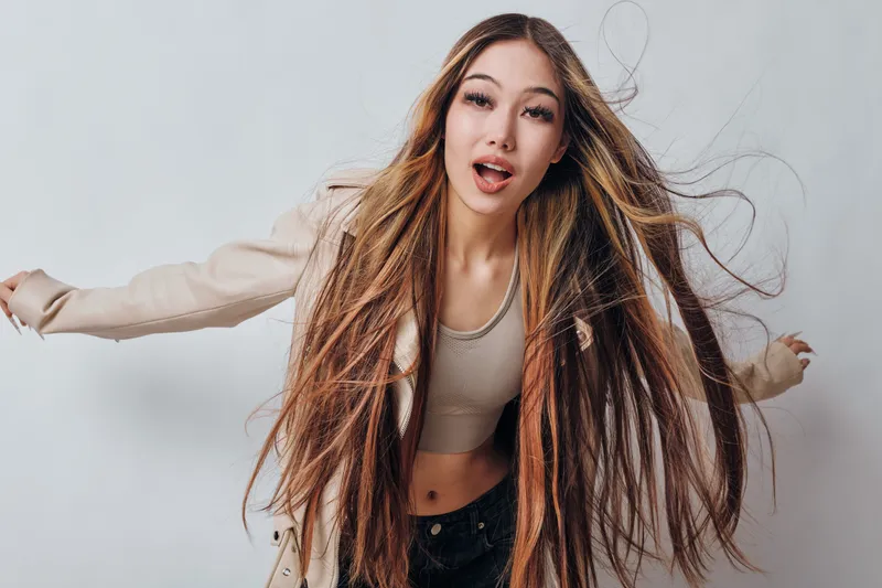 Young woman with long brown hair posing with open mouth and beige jacket against plain background, casual style, beauty and fashion portrait of female model.