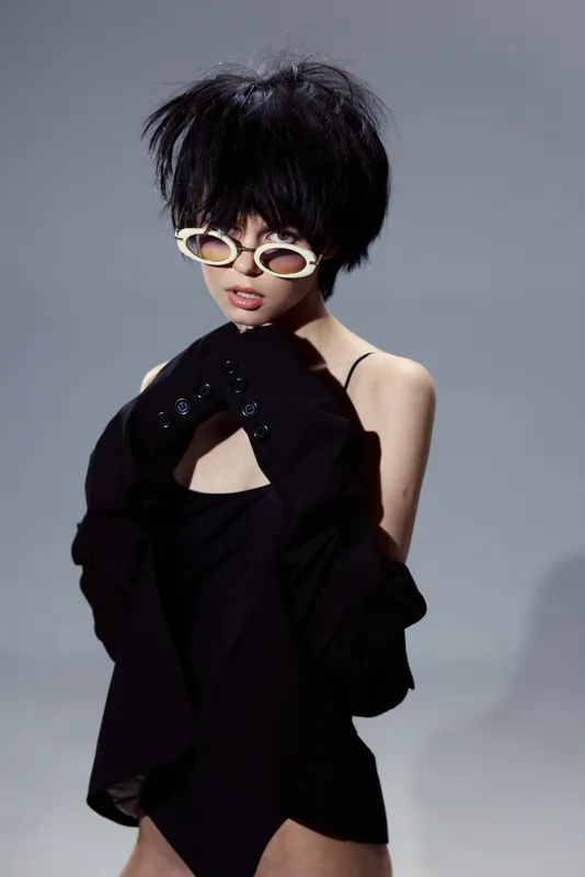 Stylish woman with short black hair wearing white sunglasses and a black outfit expressing edgy fashion and confidence