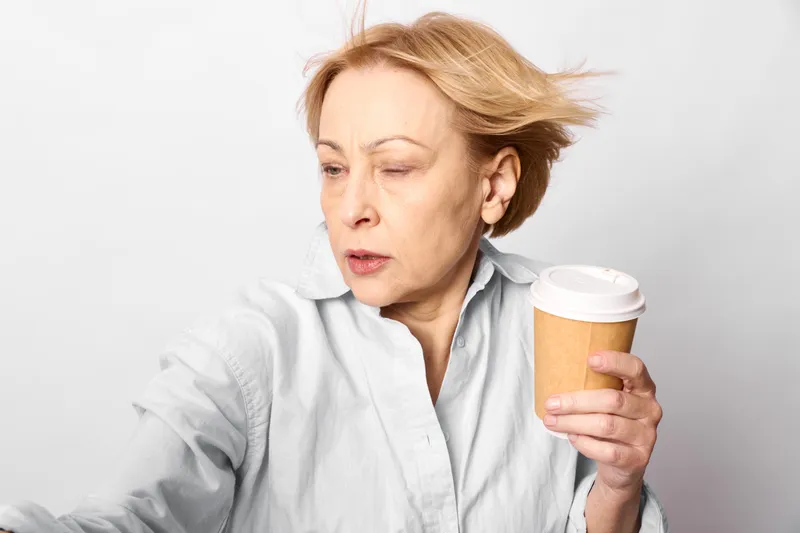 elderly woman coffee cup drinking morning relax calm portrait studio closeup, she holds a takeaway paper mug, soft light, neutral background, calm mood