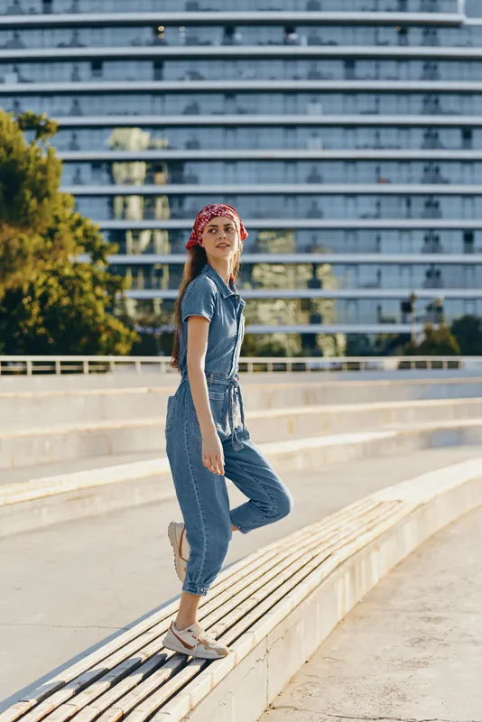 lifestyle woman in modern boho-western denim street style wearing red bandana and casual shoes in urban environment with film color effect