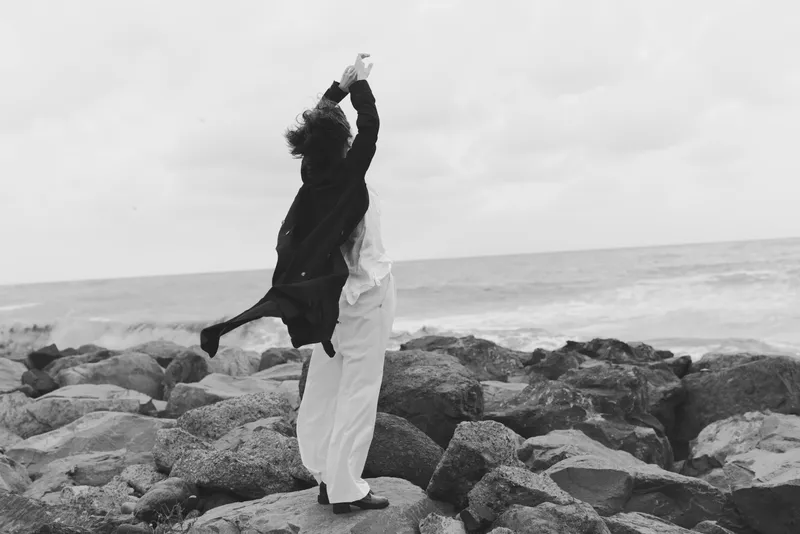 Dancing couple on a rocky shore by the sea, black and white scene capturing movement, wind in clothes, a sense of freedom and romance against rugged coast