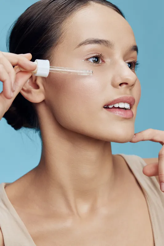 Young woman applying skincare serum on her face against a light blue background, showcasing healthy glowing skin and natural beauty Skincare, beauty, wellness