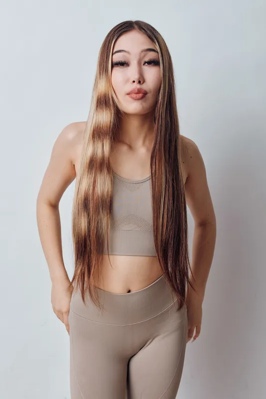 Young woman with long hair wearing sporty outfit standing with hands on hips on light background. Fitness, casual style and confident pose for health and lifestyle concept.