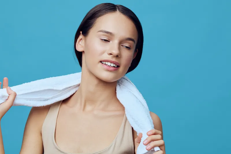 Young woman with a towel on her shoulders, smiling against a blue background, promoting healthy lifestyle and self care routines