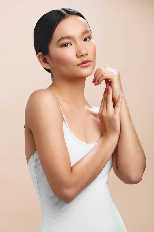 asian woman with delicate features stands in a soft studio light, calm and poised, conveying elegance and confidence for lifestyle and beauty themes. her relaxed posture and gentle gaze invite warmth