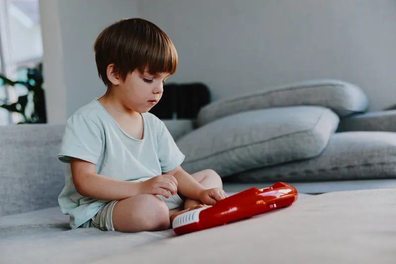 Curious boy sitting on the floor, playing with a colorful toy, exploring his surroundings with focus and joy. Bright, cozy living room creates a warm atmosphere.