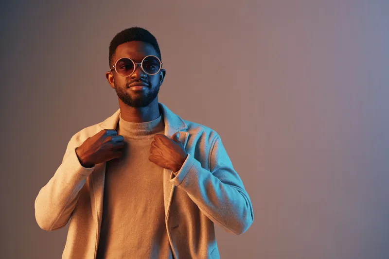 Stylish young man wearing sunglasses and a casual outfit, posing confidently against a gradient background, showcasing modern fashion and urban lifestyle