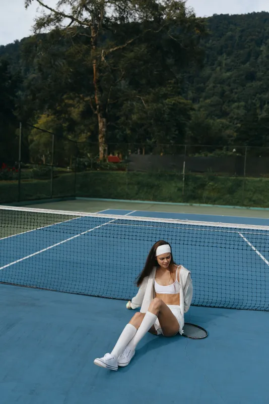 Young woman in sporty white attire smiling on a tennis court, embodying confidence and joy in a vibrant outdoor setting