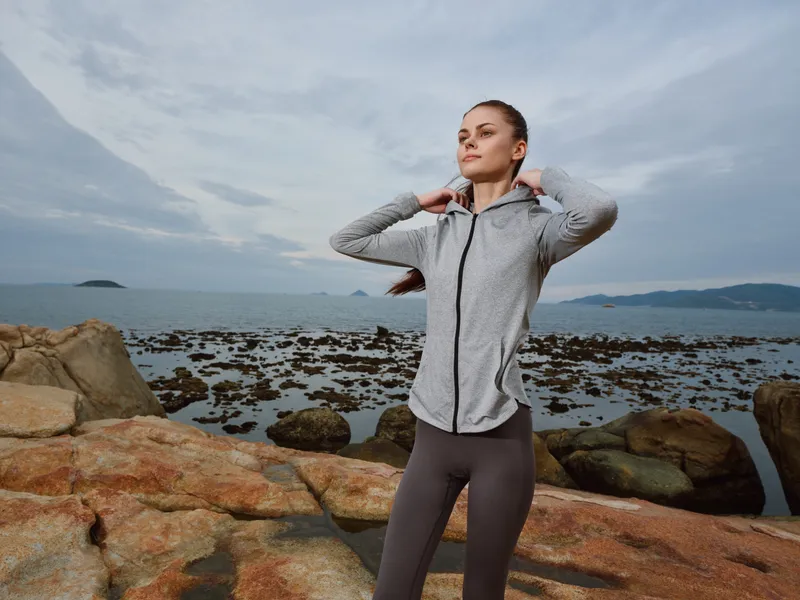 Young athletic woman wearing sportswear on a rocky beach, promoting a lifestyle of fitness and health in a serene coastal environment
