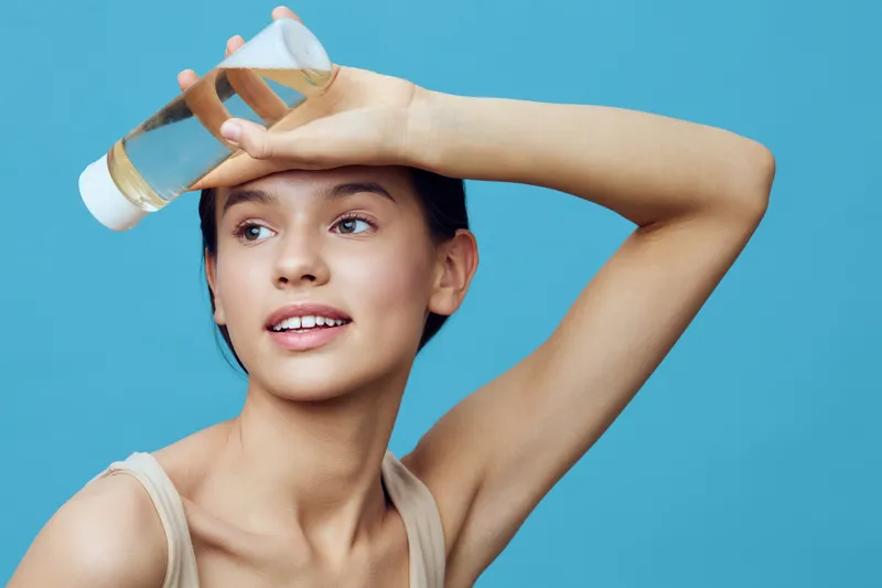 Young woman holding a bottle of oil for healthy skin on a light blue background, conveying joy and freshness, perfect for beauty and wellness concepts