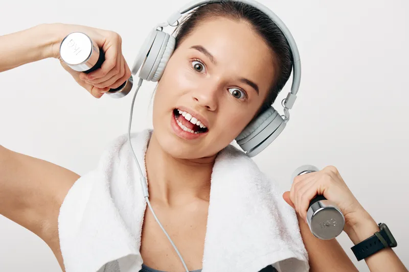 Fitness oriented woman in workout pose, lifting dumbbells with a towel around the neck and headphones, energetic training moment, athletic vibe, motivation for active lifestyle and sport.