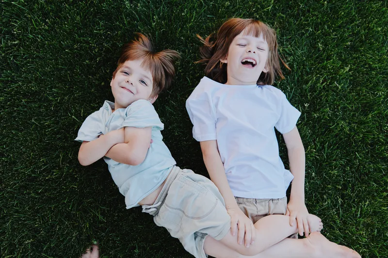 Happy children laughing on vibrant green grass, enjoying a sunny day. Their joy captures the essence of childhood innocence and playfulness.