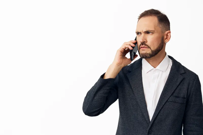 A professional man in a tailored blazer talks on a smartphone, exuding focus and confidence, isolated against a bright colored background for corporate visuals.