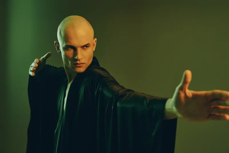 Striking man in a black robe performs a dynamic pose, showcasing strength and focus in a dramatic light setting. An artistic monochrome influence enhances the impact.