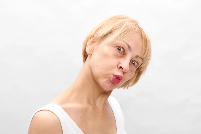 Stressed blonde woman portrait, pensive expression, lips pursed, eyes sideways, white background, concept of anxiety and mental health, emotional tension, burnout, care and support