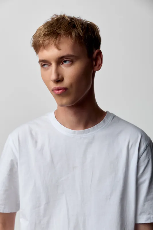 Man in white tee looking away, casual studio shot with soft lighting and clean grey backdrop, minimal style for fashion or lifestyle catalog, showcasing natural pose and relaxed mood for ecommerce use