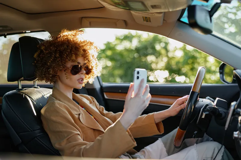 Cheerful woman indoors car self portrait, lifestyle moment with retro color film vibe, wearing sunglasses, warm interior light, casual pose, sunlit windshield, vibrant hues, candid mood