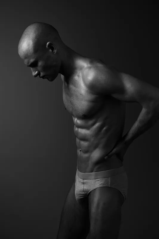 Black and white image of a contemplative man showcasing his physique, embodying strength and focus through a minimalist approach.
