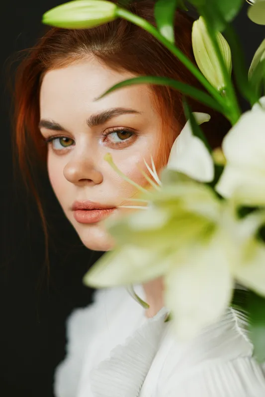 Close up portrait of a young woman with red hair, surrounded by white flowers, conveying emotional beauty and tranquility, suitable for wellness and lifestyle themes