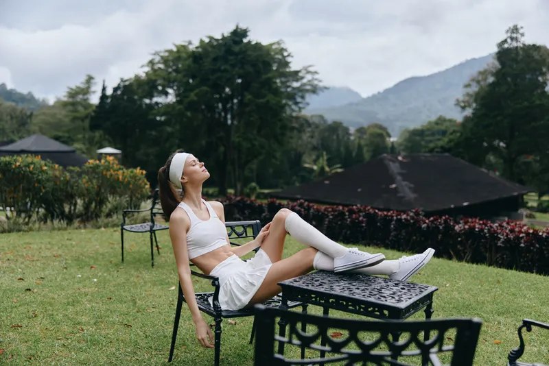 Young woman enjoying a serene outdoor moment in a white sports outfit, with mountains in the background, promoting fitness and relaxation in nature