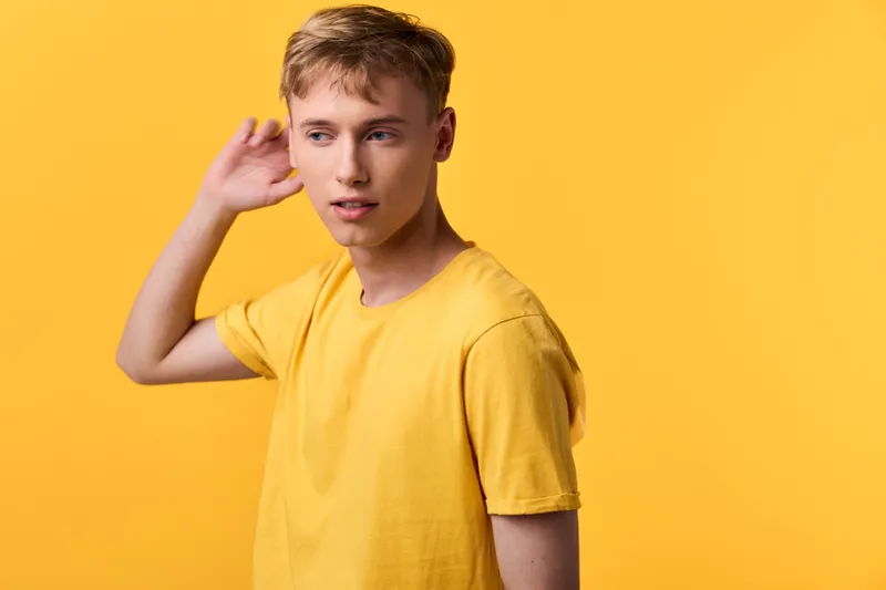 Young man in a bright yellow shirt against a vivid yellow backdrop, posing with a thoughtful glance, casual studio setup, emphasizing color harmony and relaxed style for lifestyle and fashion themes